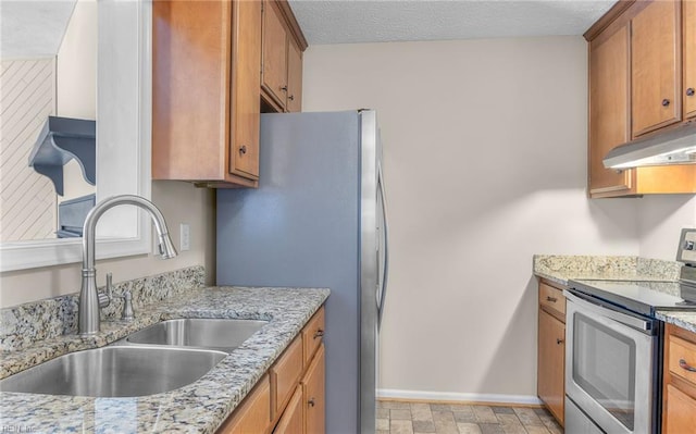 kitchen with appliances with stainless steel finishes, a sink, brown cabinetry, baseboards, and under cabinet range hood