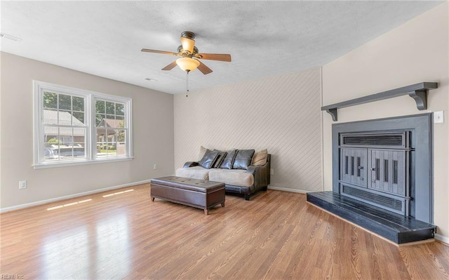 living area featuring baseboards, an accent wall, a ceiling fan, and light wood finished floors