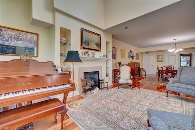 living area with a chandelier, wood finished floors, ornamental molding, a glass covered fireplace, and built in shelves