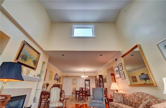 living area featuring a chandelier, a towering ceiling, wood finished floors, a glass covered fireplace, and ornamental molding