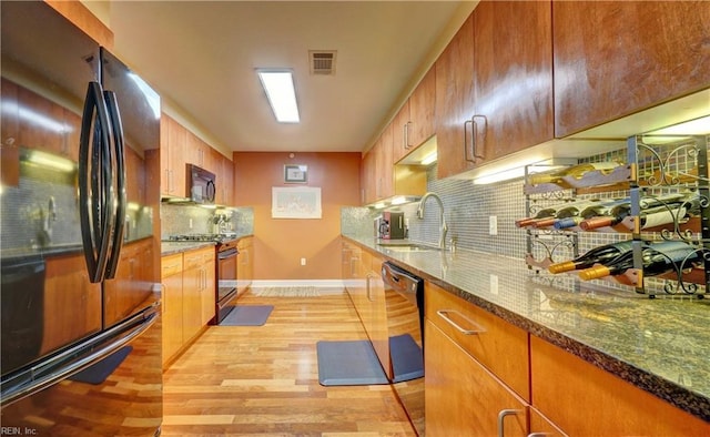 kitchen featuring black appliances, a sink, light wood finished floors, tasteful backsplash, and dark stone countertops