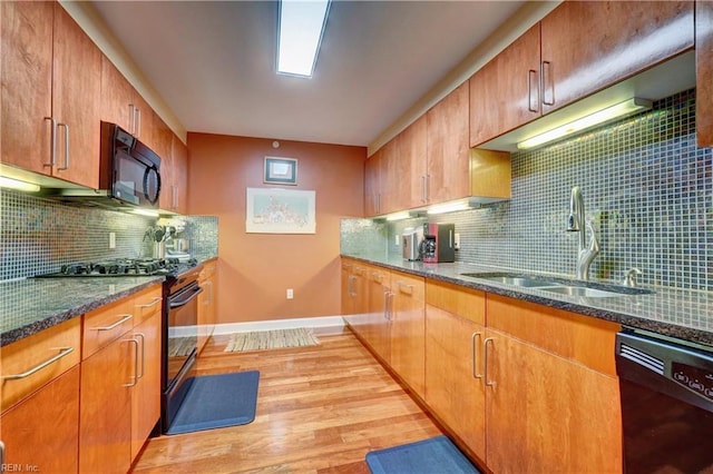 kitchen featuring black appliances, a sink, light wood-style flooring, baseboards, and tasteful backsplash