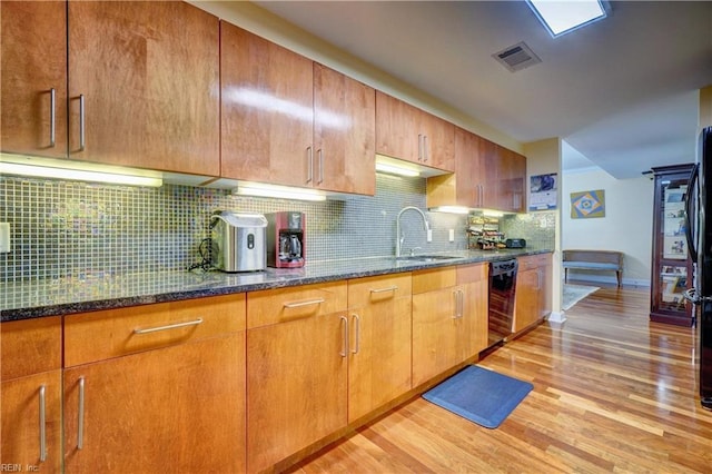 kitchen with a sink, black dishwasher, light wood finished floors, dark stone counters, and backsplash