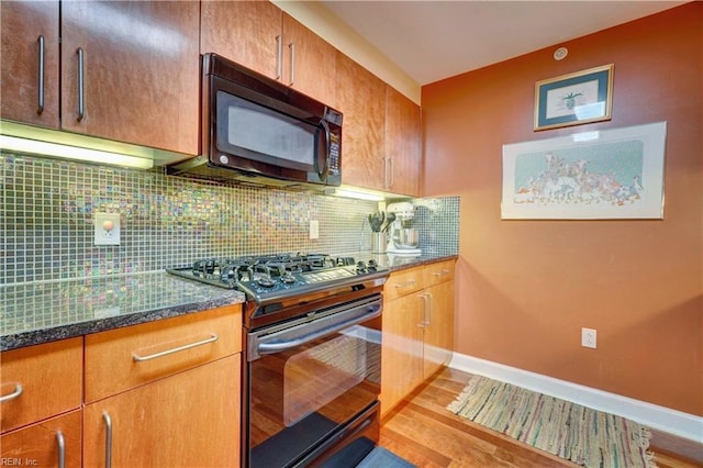 kitchen with black appliances, backsplash, light wood-type flooring, dark stone countertops, and baseboards