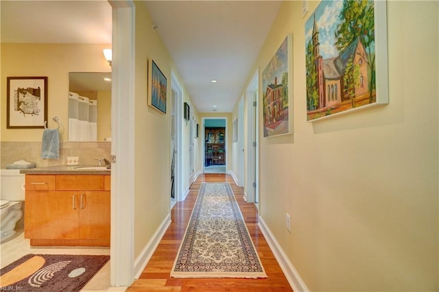hall featuring light wood-type flooring, recessed lighting, baseboards, and a sink