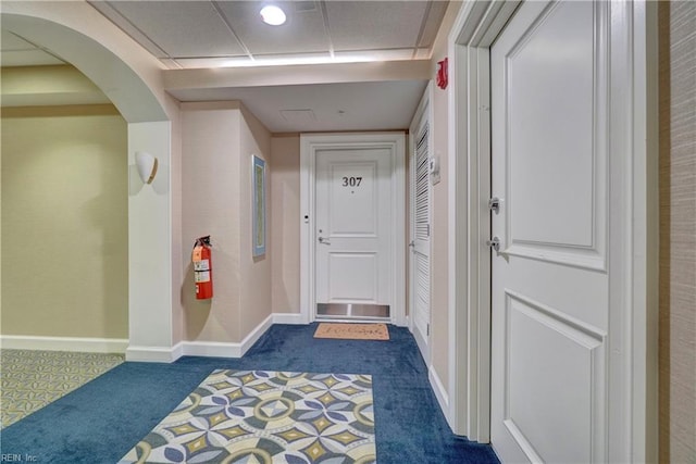 hall featuring dark carpet, baseboards, and arched walkways