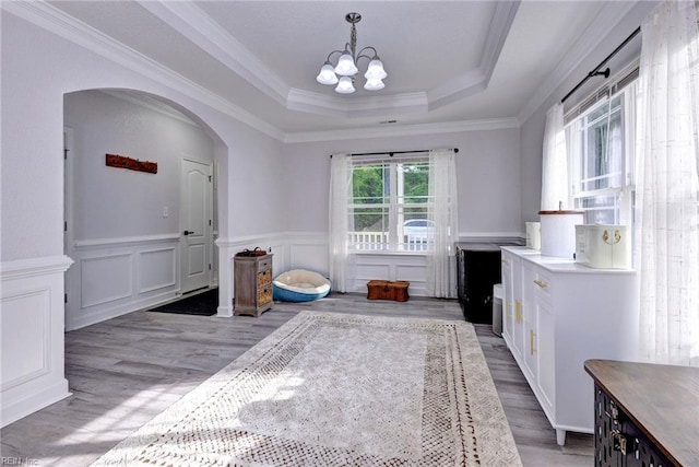 dining area featuring a wainscoted wall, arched walkways, a raised ceiling, a notable chandelier, and light wood-style floors