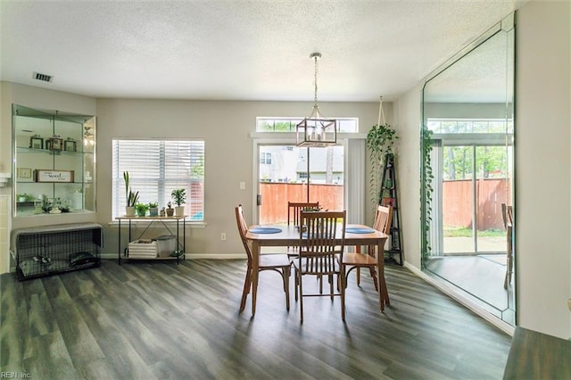 dining room with a textured ceiling, visible vents, wood finished floors, baseboards, and a chandelier