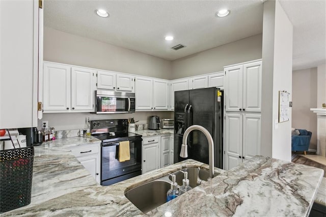 kitchen featuring visible vents, a sink, light stone counters, black appliances, and white cabinetry