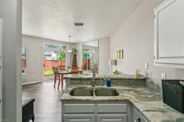 kitchen featuring a textured ceiling, visible vents, wood finished floors, a sink, and a peninsula
