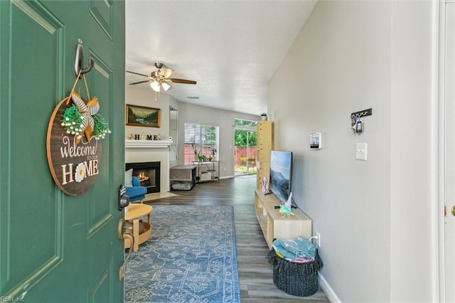 living room with baseboards, a ceiling fan, wood finished floors, and a warm lit fireplace