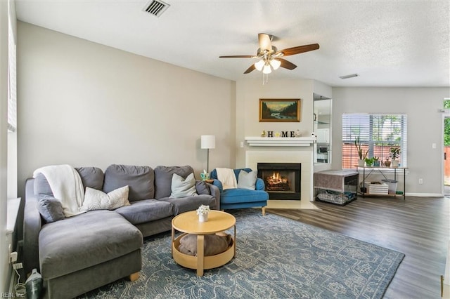 living area with ceiling fan, visible vents, a fireplace with flush hearth, and wood finished floors