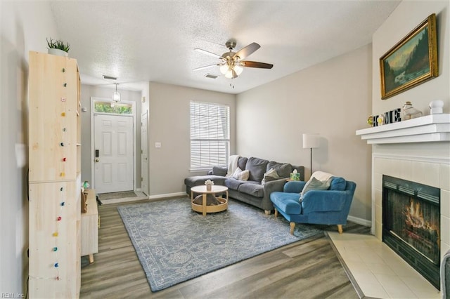 living area featuring a ceiling fan, baseboards, wood finished floors, and a fireplace