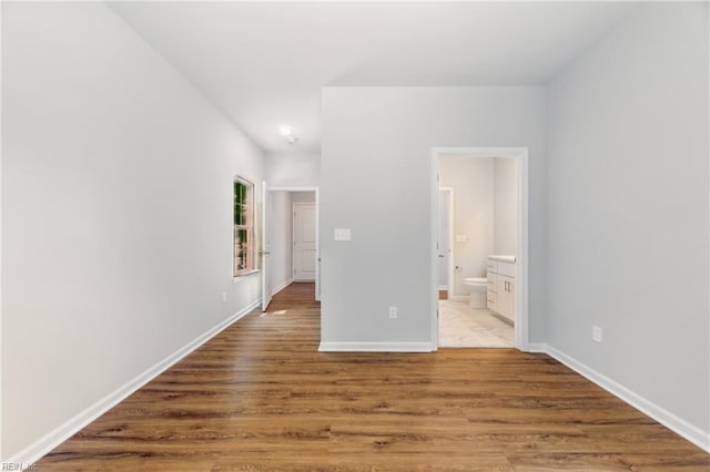 unfurnished bedroom featuring connected bathroom, baseboards, and wood finished floors