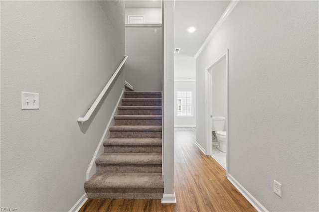 stairs with crown molding, baseboards, a textured wall, and wood finished floors