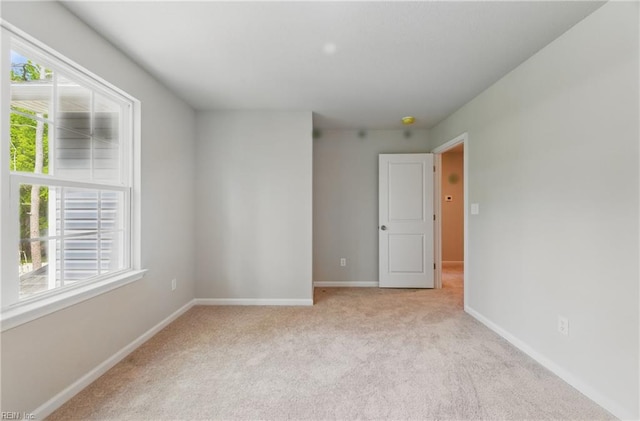 spare room featuring light colored carpet, baseboards, and a wealth of natural light