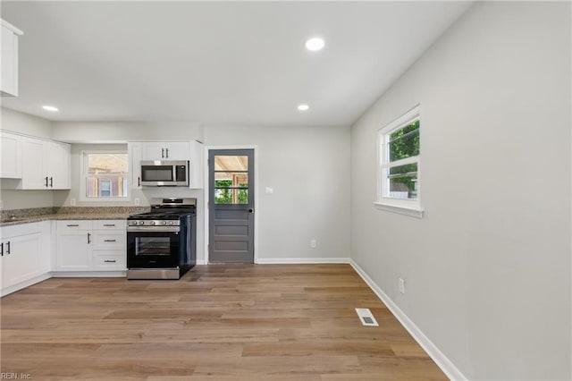 kitchen featuring visible vents, baseboards, white cabinets, light wood finished floors, and appliances with stainless steel finishes