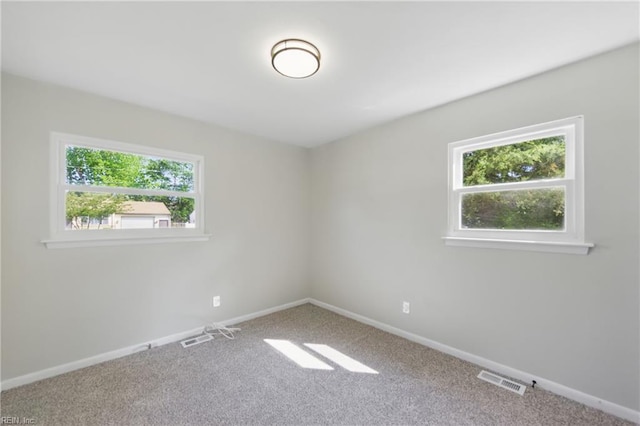 carpeted empty room featuring baseboards, visible vents, and a wealth of natural light