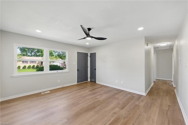 unfurnished room featuring a ceiling fan, attic access, visible vents, light wood-type flooring, and baseboards