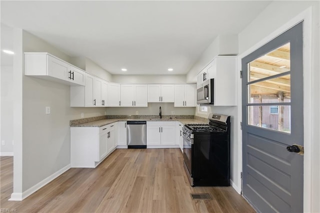 kitchen featuring white cabinets, appliances with stainless steel finishes, a sink, baseboards, and light wood-type flooring