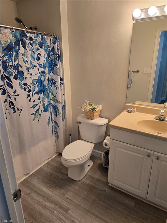 bathroom featuring toilet, curtained shower, wood finished floors, and vanity