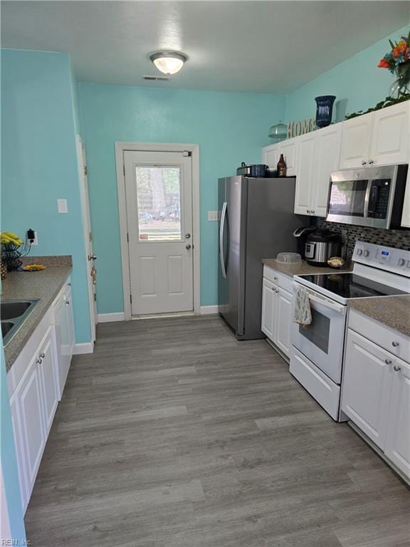 kitchen with stainless steel microwave, light wood-type flooring, white cabinets, and electric range