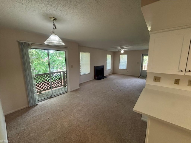 unfurnished living room with baseboards, ceiling fan, light colored carpet, a textured ceiling, and a fireplace with flush hearth