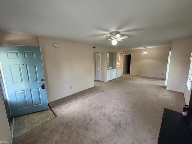 unfurnished living room with a ceiling fan, baseboards, and light carpet