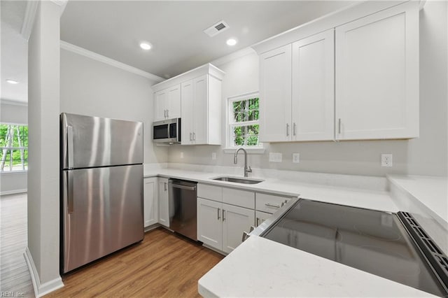 kitchen featuring appliances with stainless steel finishes, a sink, light wood-style floors, visible vents, and ornamental molding