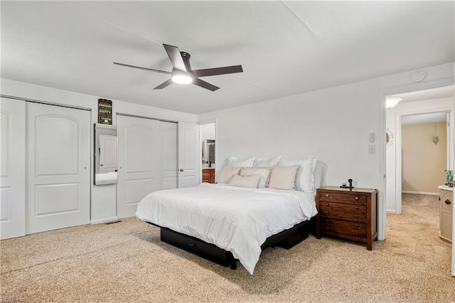 bedroom with light colored carpet, multiple closets, and ceiling fan