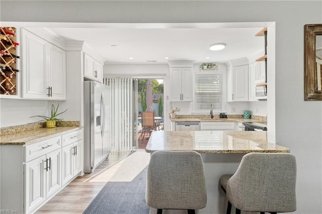 kitchen featuring a sink, light stone counters, a breakfast bar, stainless steel appliances, and white cabinetry