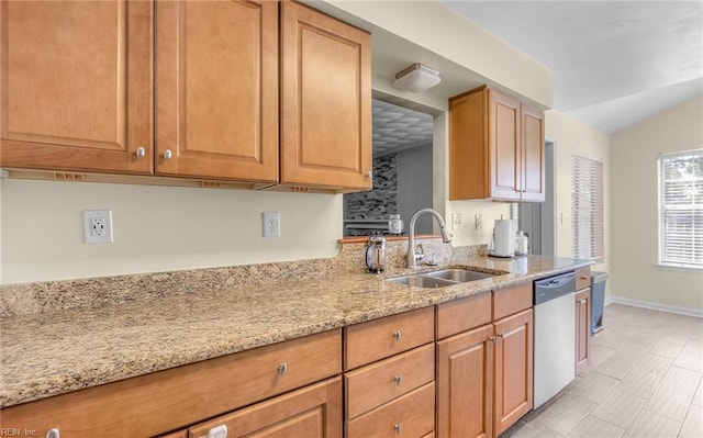 kitchen featuring vaulted ceiling, dishwasher, a sink, light stone counters, and baseboards