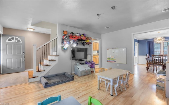 living area featuring visible vents, a chandelier, light wood-style flooring, and stairway