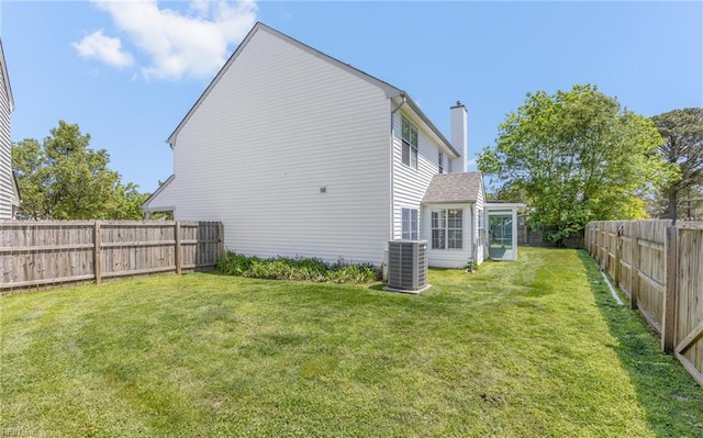 rear view of property featuring a lawn, a chimney, central AC, and a fenced backyard