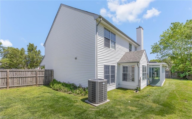 rear view of house featuring a yard, central AC, a chimney, and a fenced backyard