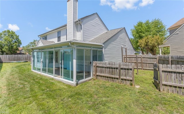 back of house featuring a chimney, a lawn, a sunroom, a fenced backyard, and a shingled roof