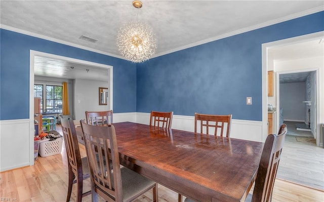 dining space featuring an inviting chandelier, light wood finished floors, a wainscoted wall, visible vents, and ornamental molding
