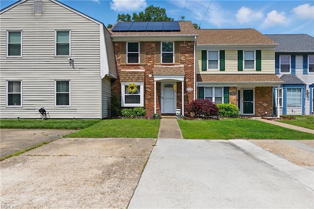 multi unit property featuring brick siding, solar panels, and a front yard