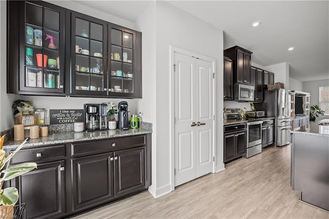 kitchen featuring glass insert cabinets, light wood-style flooring, stainless steel appliances, light stone countertops, and recessed lighting