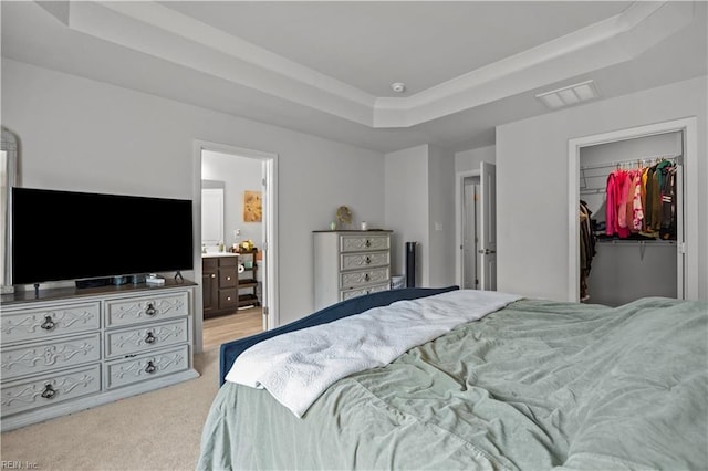 bedroom with a closet, a tray ceiling, visible vents, a walk in closet, and light colored carpet