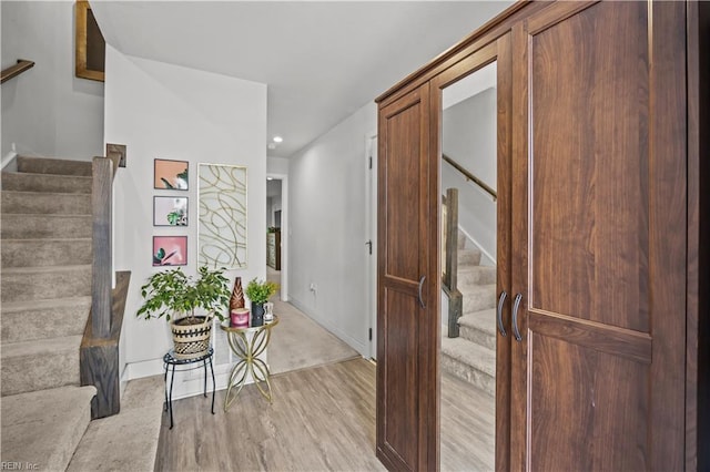 corridor with recessed lighting, light wood-style flooring, baseboards, and stairs