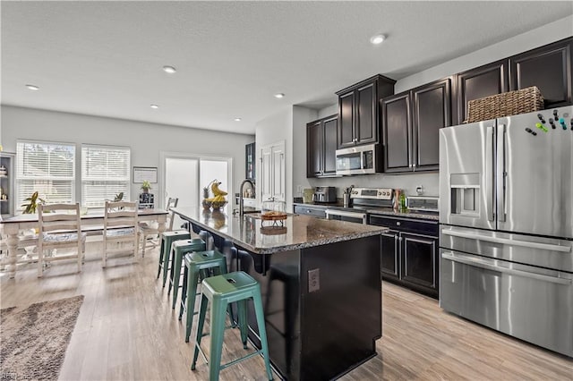 kitchen featuring light wood-type flooring, stainless steel appliances, an island with sink, and a sink