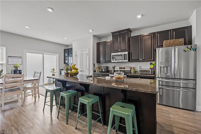 kitchen with a sink, a breakfast bar, an island with sink, light wood finished floors, and appliances with stainless steel finishes