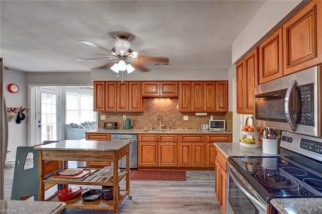 kitchen featuring ceiling fan, brown cabinetry, appliances with stainless steel finishes, a sink, and light wood-style flooring