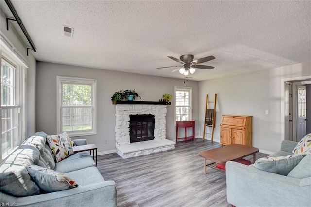 living room with ceiling fan, a textured ceiling, visible vents, wood finished floors, and baseboards