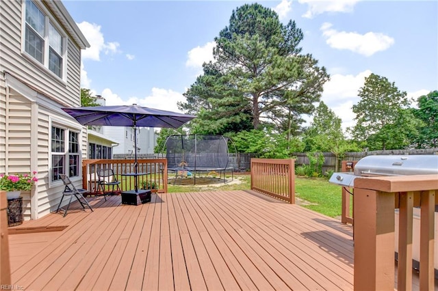 wooden deck featuring a fenced backyard, a trampoline, and a yard