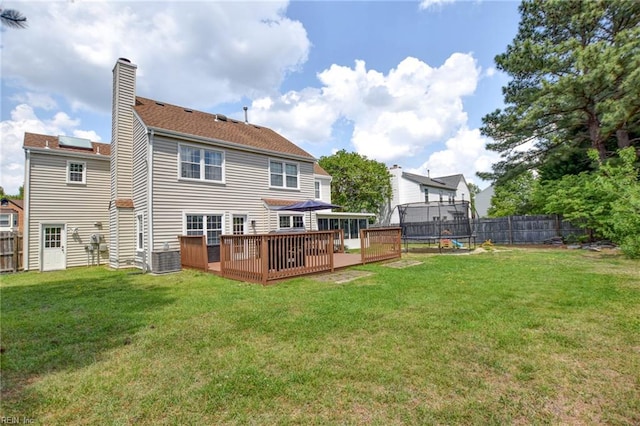 rear view of property featuring a deck, fence, a chimney, and a trampoline