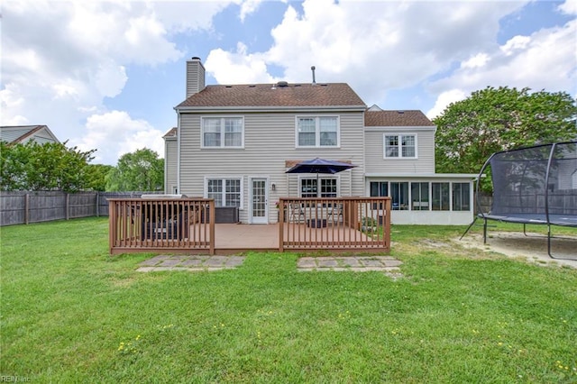 rear view of house with a trampoline, a wooden deck, a sunroom, a fenced backyard, and a yard