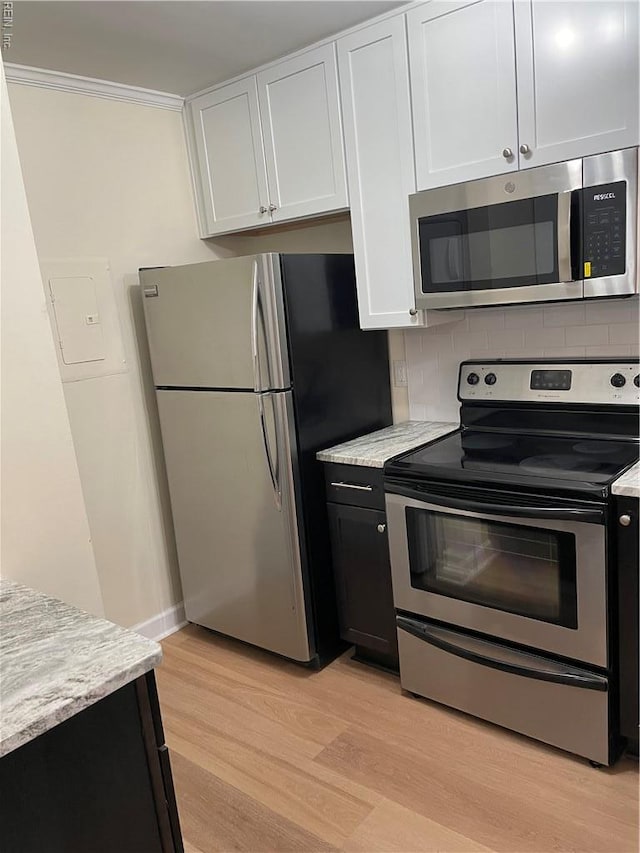 kitchen with ornamental molding, light wood-style floors, white cabinetry, appliances with stainless steel finishes, and backsplash