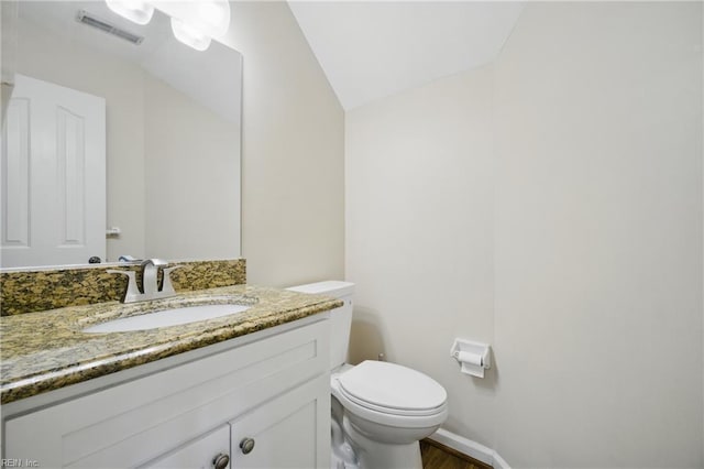 half bathroom featuring visible vents, vaulted ceiling, wood finished floors, vanity, and toilet
